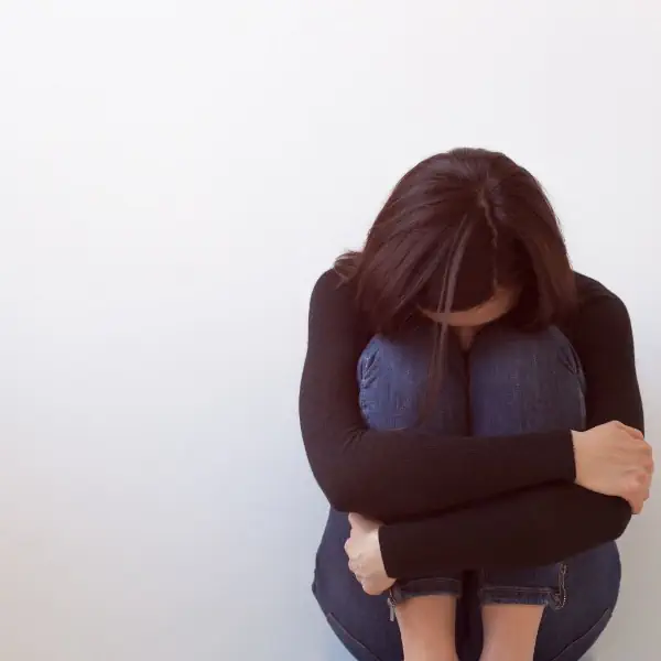 Mujer afligida, sentada cubriendo la cara con sus rodillas